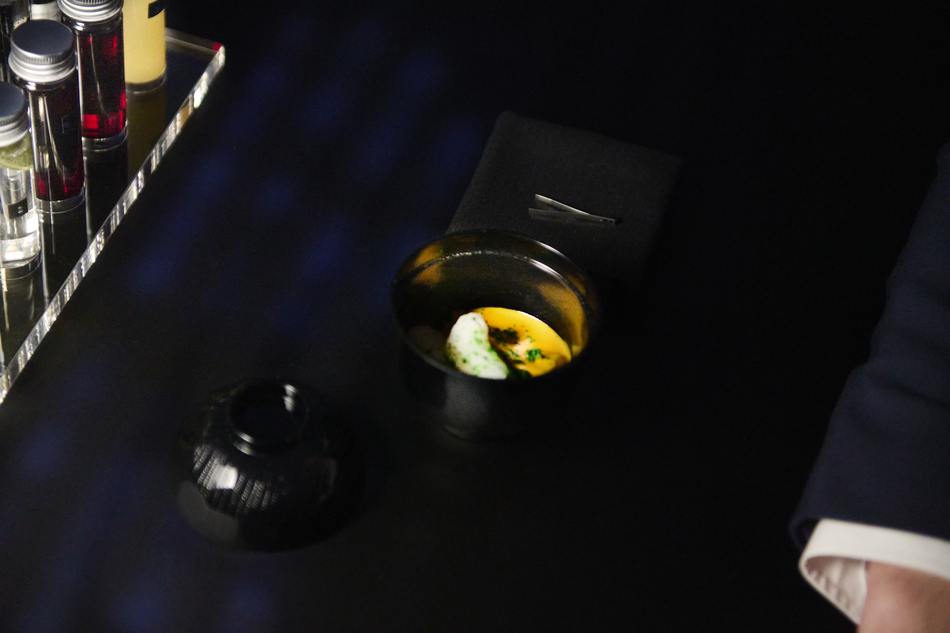 A course served in a dark bowl on the black surface of the table, lit only from within the table