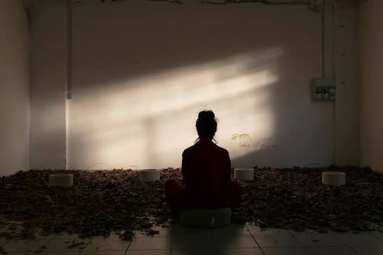 A scent installation by SOM Perfume: a figure seated in a dark room among fallen leaves and open vessels